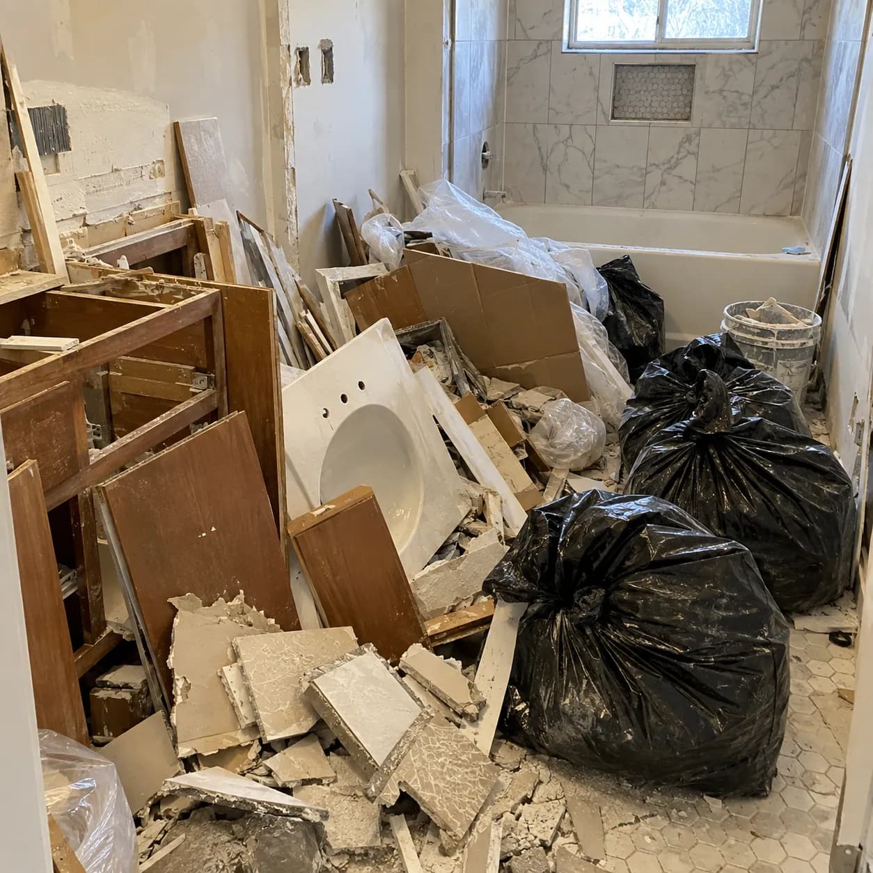 A stripped-out bathroom with the old sink, vanity panels and broken board stacked on the floor